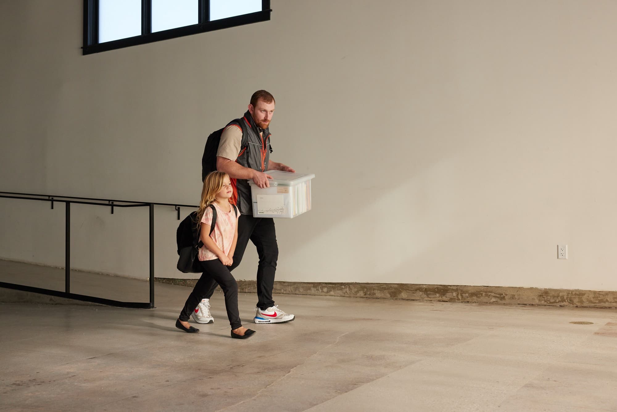 A father wearing a Perci Vest carries a box out, his daughter beside him